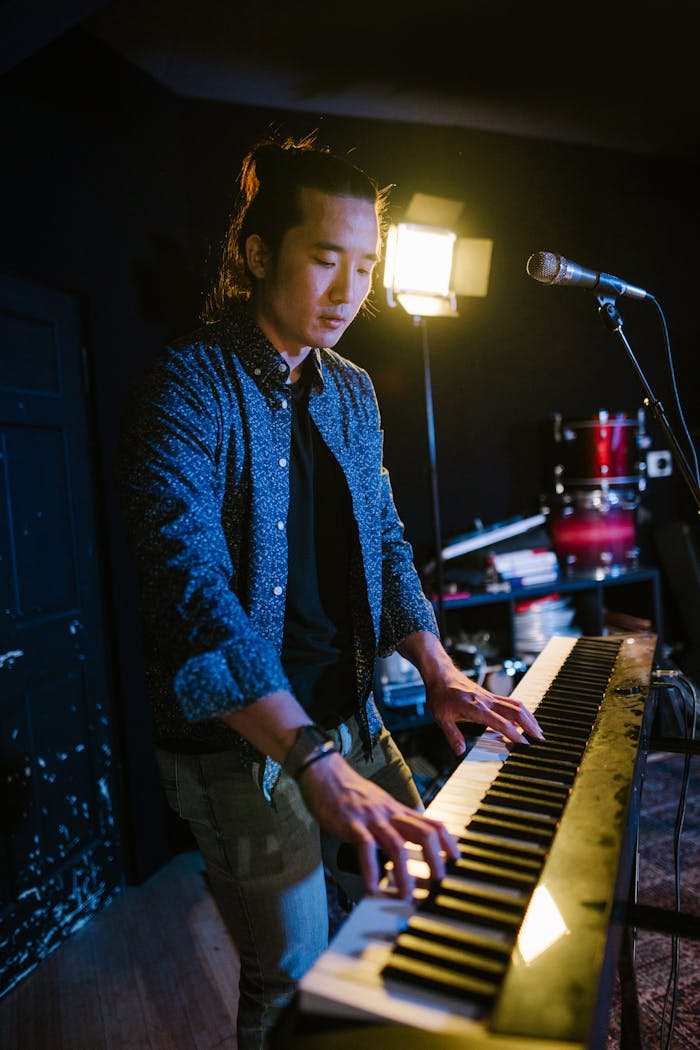 A musician rehearses with a piano and microphone under stage lights.